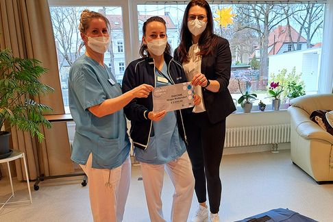 Drei Mitarbeiterinnen bei der Übergabe von der Firma SOFTLINE-Schaum GmbH & Co. KG gespendetem 7-teiligen Set verschiedener Positionshilfen.
