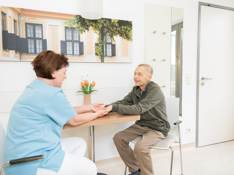 Pflegerin Patient sitzen an einem Tisch und halten sich die Hände
