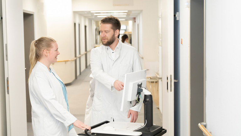 Prof. Dr. med. Torsten Diekhoff spricht mit einer Medizinstudentin an einem mobilen Visitenwagen auf dem Flur - Immanuel Klinik Rüdersdorf  - Nachricht - Weiterbildungsbefugnisse stärken ärztlichen Nachwuchs in Rüdersdorf