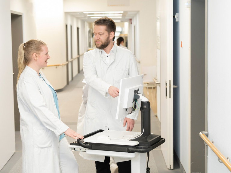Prof. Dr. med. Torsten Diekhoff spricht mit einer Medizinstudentin an einem mobilen Visitenwagen auf dem Flur - Immanuel Klinik Rüdersdorf  - Nachricht - Weiterbildungsbefugnisse stärken ärztlichen Nachwuchs in Rüdersdorf