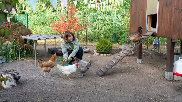 Eine Frau hockt auf dem Boden und hat mehrere Hühner in einem Gehege um sich herum im Diakonie Hospiz Woltersdorf